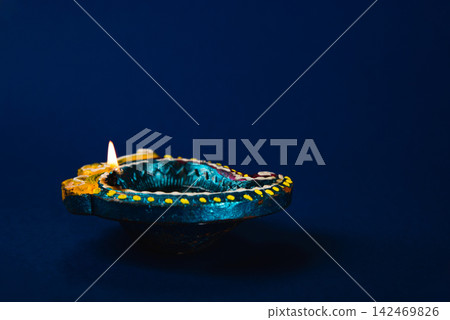 Diwali and Holi celebration with glowing clay diya lamps. Shiny and vibrant, these lamps symbolize happiness, prosperity, and spirituality. Perfect for festive invitations, a blue background. Diwali and Holi celebration with glowing clay diya lamps. Shiny and vibrant, these lamps symbolize happiness, prosperity, and spirituality. Perfect for festive invitations, a blue background. 142469826