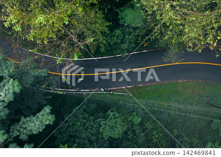 aerial view of a winding asphalt road cutting through a lush green forest covered in mist. 142469841