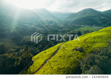 Aerial view of a scenic dirt trail leading up a vibrant green grassy hill in a lush mountain valley. Aerial view of a scenic dirt trail leading up a vibrant green grassy hill in a lush mountain valley. 142469848