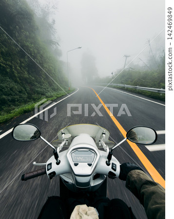 POV shot of riding a scooter on a wet, winding mountain road through a dense, foggy forest. 142469849