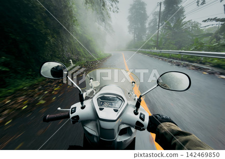 POV shot of riding a scooter on a wet, winding mountain road through a dense, foggy forest. POV shot of riding a scooter on a wet, winding mountain road through a dense, foggy forest. 142469850