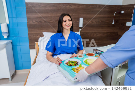 Nurse in medical coat is holding a tray with breakfast for the young female patient. Nurse in medical coat is holding a tray with breakfast for the young female patient. 142469951