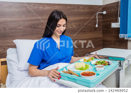 Tray with breakfast for the young female patient. The young woman eating in the hospital. 142469952