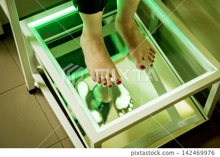 Doctor is at examining womans feet by using plantoscopy device Doctor is at examining womans feet by using plantoscopy device 142469976