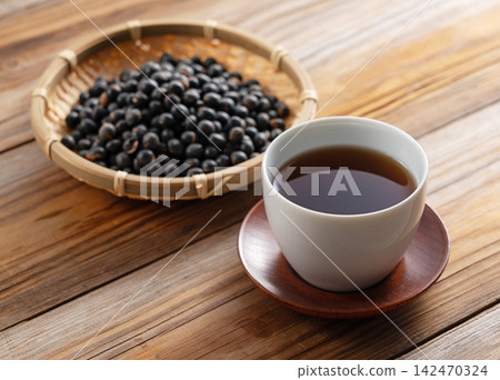 木桌上擺放著黑豆茶,竹籃裡盛著烤黑豆。這是日本養生茶飲和生活方式的展現。 木桌上擺放著黑豆茶,竹籃裡盛著烤黑豆。這是日本養生茶飲和生活方式的展現。 142470324