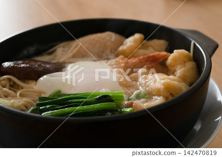 一碗鍋燒烏冬面,上面放著雞蛋和炸蝦天婦羅。 一碗鍋燒烏冬面,上面放著雞蛋和炸蝦天婦羅。 142470819