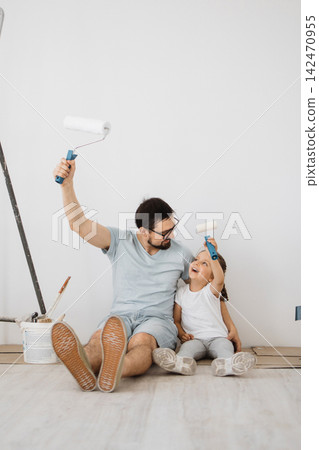 A father and his young daughter sit on the floor, holding paint rollers and smiling at each other during a home renovation project A father and his young daughter sit on the floor, holding paint rollers and smiling at each other during a home renovation project 142470955