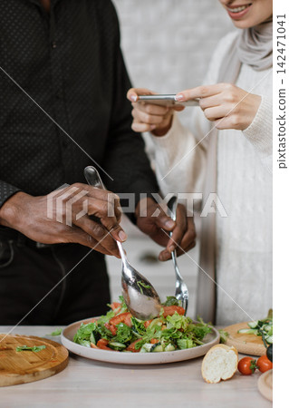 A man and woman are preparing a fresh salad, with the woman capturing the moment on her smartphone A man and woman are preparing a fresh salad, with the woman capturing the moment on her smartphone 142471041