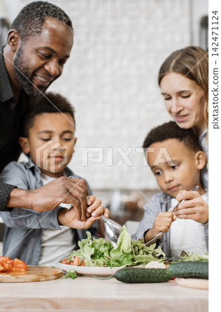 A diverse family happily makes a fresh salad in the kitchen, teaching children about healthy eating A diverse family happily makes a fresh salad in the kitchen, teaching children about healthy eating 142471124