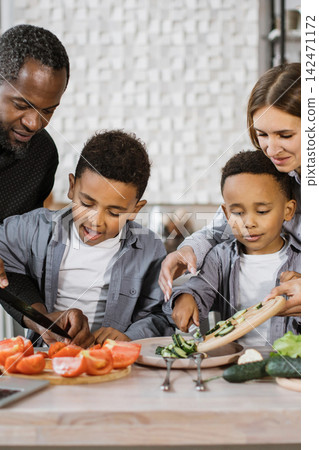 A diverse family is happily preparing a healthy meal together in a bright, modern kitchen, chopping fresh vegetables for a salad A diverse family is happily preparing a healthy meal together in a bright, modern kitchen, chopping fresh vegetables for a salad 142471172