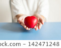 Close up of hands holding red heart on blue background for charity and healthcare concept 142471248