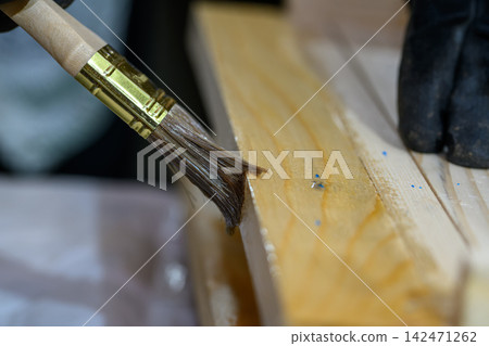 hand holding a brush applying varnish paint on a wooden garden table - painting and caring for wood with oil - shallow depth of field - focus on brush hand holding a brush applying varnish paint on a wooden garden table - painting and caring for wood with oil - shallow depth of field - focus on brush 142471262