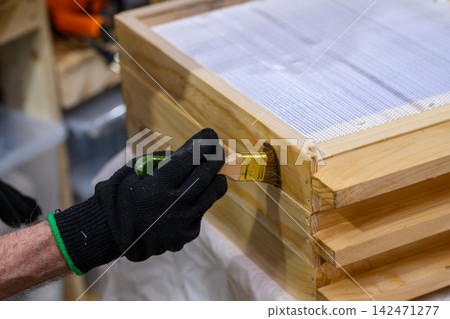 hand holding a brush applying varnish paint on a wooden garden table - painting and caring for wood with oil - shallow depth of field - focus on brush hand holding a brush applying varnish paint on a wooden garden table - painting and caring for wood with oil - shallow depth of field - focus on brush 142471277
