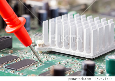 Red multimeter probe testing electronic components on a green circuit board with a silver heatsink Red multimeter probe testing electronic components on a green circuit board with a silver heatsink 142471528