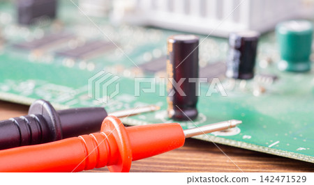 Red and black multimeter probes lying in front of a blurred green electronic circuit board Red and black multimeter probes lying in front of a blurred green electronic circuit board 142471529