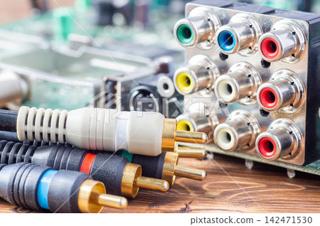 RCA cables with gold-plated connectors lying next to an analog audio-video jack panel RCA cables with gold-plated connectors lying next to an analog audio-video jack panel 142471530