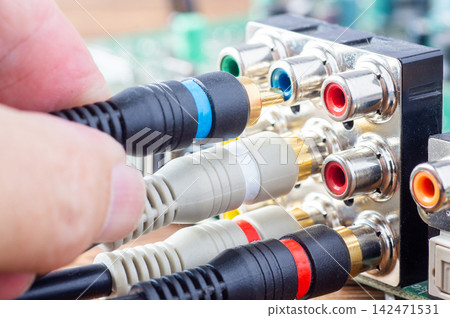 Hand plugging a blue RCA cable into an analog audio-video connector panel on a circuit board Hand plugging a blue RCA cable into an analog audio-video connector panel on a circuit board 142471531