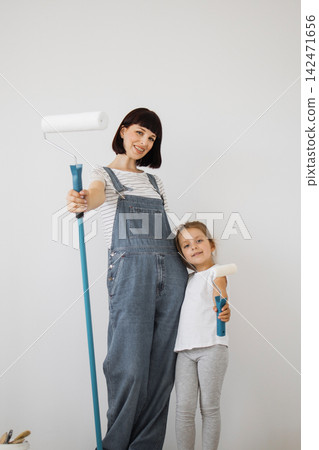 A woman and a young girl in overalls stand side-by-side holding paint rollers, ready to redecorate a room A woman and a young girl in overalls stand side-by-side holding paint rollers, ready to redecorate a room 142471656