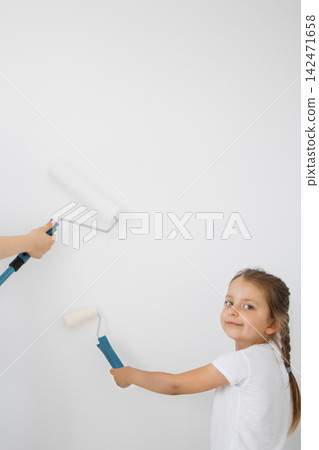 A young girl and an adult hand hold paint rollers to a white wall, suggesting a home improvement project or creative activity A young girl and an adult hand hold paint rollers to a white wall, suggesting a home improvement project or creative activity 142471658