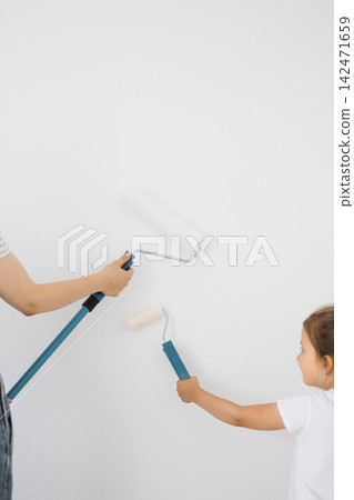 A parent and child are painting a white wall with rollers, engaging in a home improvement activity 142471659