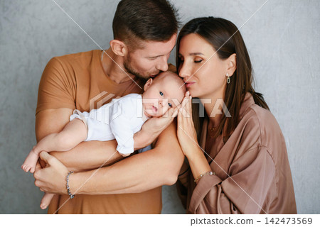 Parents Kissing Baby While Holding Together 142473569
