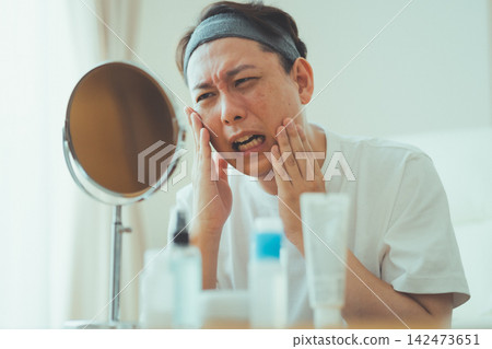 A 40-year-old man touches his cheeks with both hands in front of the mirror and is shocked by his aging face - Men's Beauty A 40-year-old man touches his cheeks with both hands in front of the mirror and is shocked by his aging face - Men's Beauty 142473651