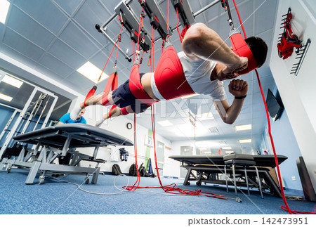 Physiotherapy. Suspension training therapy. Young man doing fitness traction therapy with suspension-based exercise training system. Physiotherapy. Suspension training therapy. Young man doing fitness traction therapy with suspension-based exercise training system. 142473951