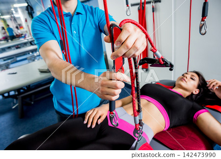 Physiotherapy. Suspension training therapy. Young woman doing fitness traction therapy with suspension-based exercise training system. Physiotherapy. Suspension training therapy. Young woman doing fitness traction therapy with suspension-based exercise training system. 142473990