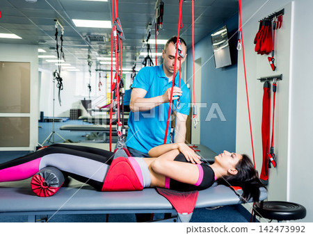 Physiotherapy. Suspension training therapy. Young woman doing fitness traction therapy with suspension-based exercise training system. Physiotherapy. Suspension training therapy. Young woman doing fitness traction therapy with suspension-based exercise training system. 142473992