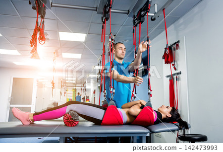 Physiotherapy. Suspension training therapy. Young woman doing fitness traction therapy with suspension-based exercise training system. 142473993