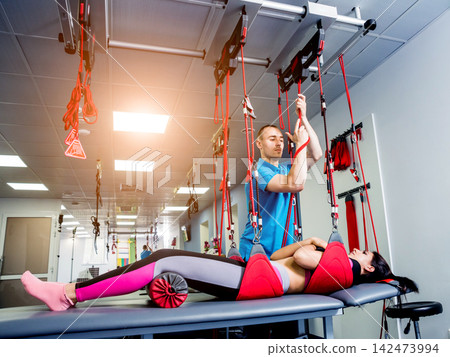 Physiotherapy. Suspension training therapy. Young woman doing fitness traction therapy with suspension-based exercise training system. Physiotherapy. Suspension training therapy. Young woman doing fitness traction therapy with suspension-based exercise training system. 142473994