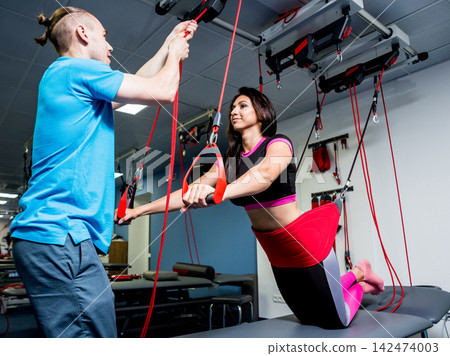 Physiotherapy. Suspension training therapy. Young woman doing fitness traction therapy with suspension-based exercise training system. Physiotherapy. Suspension training therapy. Young woman doing fitness traction therapy with suspension-based exercise training system. 142474003