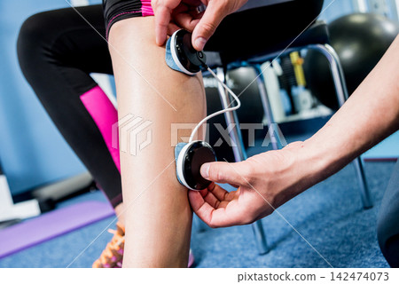 Physical therapist install electrostimulator on the muscles of the legs. Fitness training with an electrostimulator. Physical therapist install electrostimulator on the muscles of the legs. Fitness training with an electrostimulator. 142474073