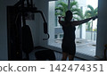 Dramatic dark silhouette of young woman with arms spread wide lifting dumbbells laterally in a brightly backlit gym interior. Power and strength concept 142474351