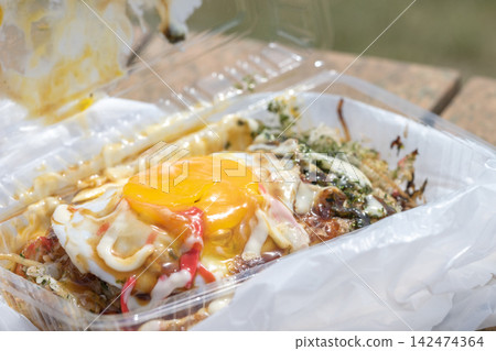 A packaged street food item topped with a fried egg. A packaged street food item topped with a fried egg. 142474364