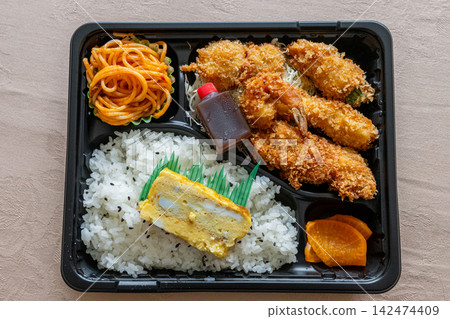 A hearty bento box featuring fried shrimp and egg rolls. A hearty bento box featuring fried shrimp and egg rolls. 142474409