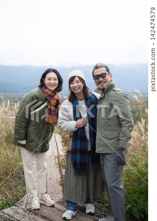 三個朋友依偎在鋪滿秋葉的木板路上。 142474579