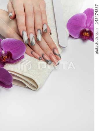 Woman receiving manicure treatment with orchids and nail file Woman receiving manicure treatment with orchids and nail file 142474887