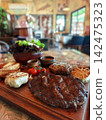 Grilled Tomahawk and Ribeye Steak Platter with Potato Wedges and Salad 142475323