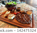 Grilled Tomahawk and Ribeye Steak Platter with Potato Wedges and Salad 142475324