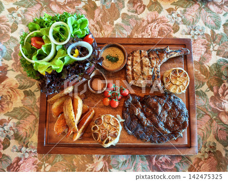 Grilled Tomahawk and Ribeye Steak Platter with Potato Wedges and Salad Grilled Tomahawk and Ribeye Steak Platter with Potato Wedges and Salad 142475325