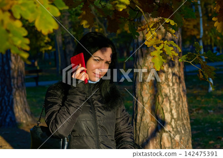 Woman calling,talking,listening while walking in an autumn park Woman calling,talking,listening while walking in an autumn park 142475391