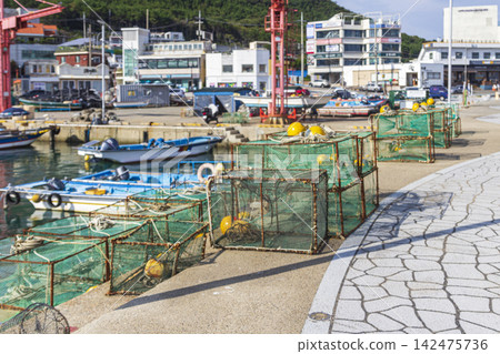 Numerous small fishing boats and stacked net traps fill a working harbor beside a dense urban waterfront. Numerous small fishing boats and stacked net traps fill a working harbor beside a dense urban waterfront. 142475736