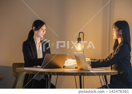 Two female business professionals open documents and hold a meeting. Two female business professionals open documents and hold a meeting. 142476301