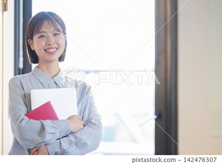 一位女士面帶微笑，將筆記型電腦和筆記本抱在胸前。 142476307