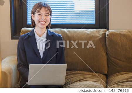 一位女士坐在沙發上，膝上放著一台筆記型電腦，她笑著看著這一切。 142476313