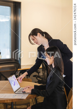 一位女老闆/資深同事一邊指導一位年輕同事，一邊指著螢幕。 142476314