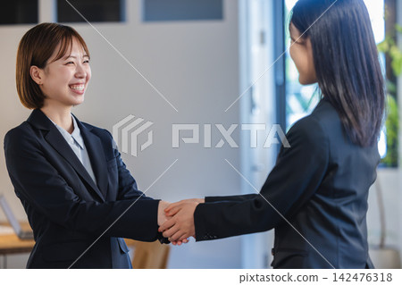 辦公室裡,兩位女性專業人士微笑著握手。 辦公室裡,兩位女性專業人士微笑著握手。 142476318