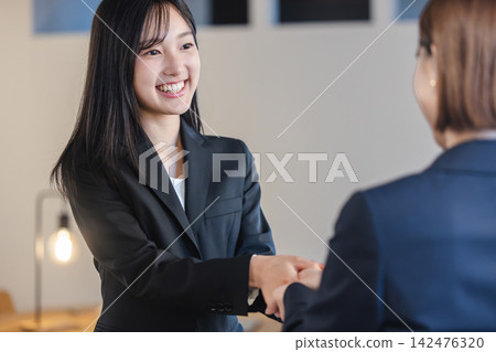 Female business people exchanging handshakes with smiles. Female business people exchanging handshakes with smiles. 142476320