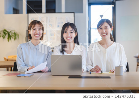 A team of female employees smiling in a bright office. A team of female employees smiling in a bright office. 142476335